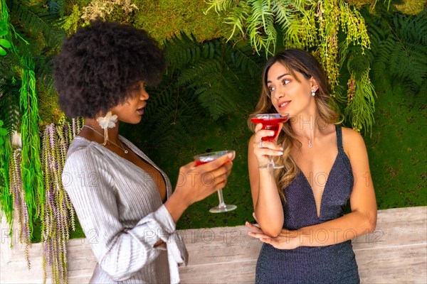 Two friends in gala dresses having a cocktail at a party in a hotel