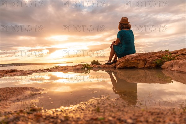 A young tourist sitting at sunset on the paseo de poniente in San Antonio Abad