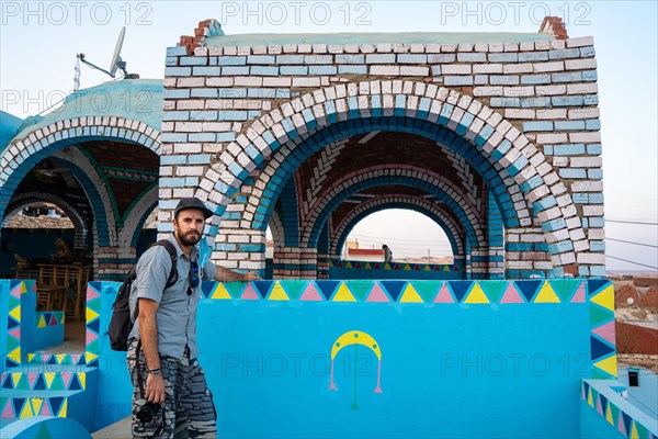 A young tourist sitting on a beautiful terrace of a traditional blue house in a Nubian village along the Nile river and near the city of Aswan. Egypt