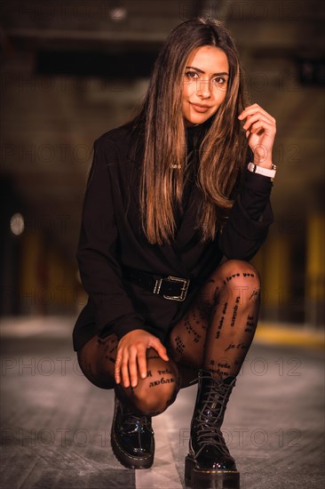 Young caucasian brunette with black jacket in an empty underground car park. Night urban session in the city