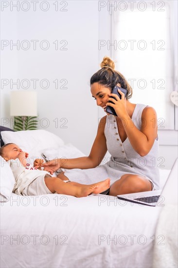 Young Caucasian mother with her son in the room on top of the bed. Mother teleworking and caring for her child