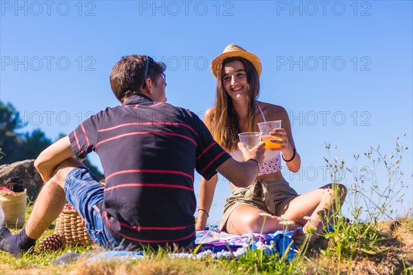 A young Caucasian couple at the picnic drinking orange juice in the mountains by the sea enjoying the heat