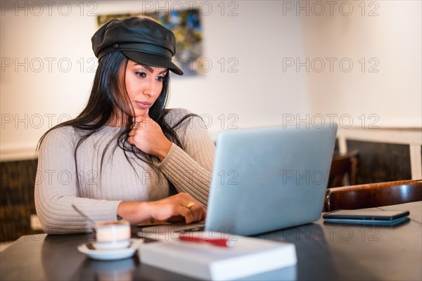 Latina brunette architect reading work emails with computer teleworking from a cafeteria