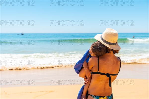 Mother with hat hugging and having fun with her son by the sea