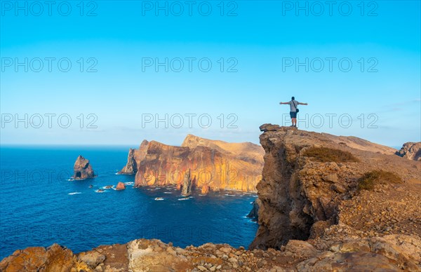 A young man on a cliff at Ponta de Sao Lourenco on the coast with rock formations in summer