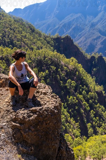 A young woman resting after trekking on top of La Cumbrecita sitting in the natural viewpoint looking at the mountains of the Caldera de Taburiente