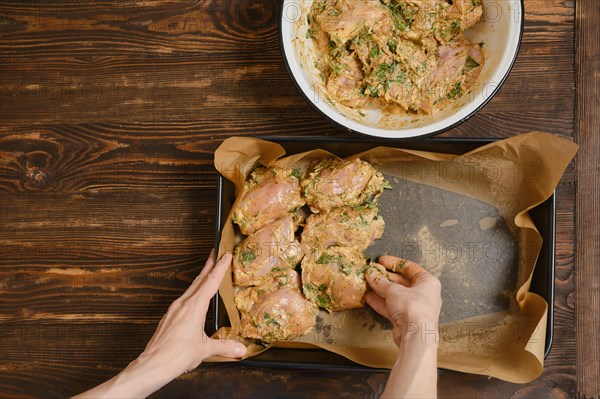 Hands of woman putting chicken thighs in baking tray from a bowl