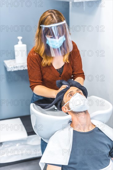 Reopening of hairdressing salons after the Coronavirus pandemic. Hairdresser with face mask and protective screen