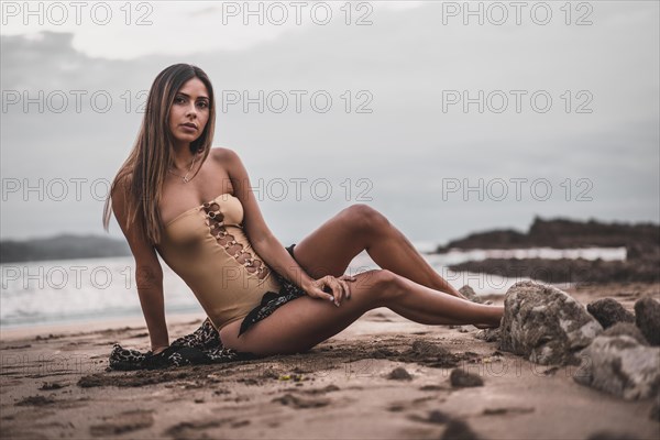 Fashion posing of a brunette woman in a swimsuit and a pareo on the beach in summer