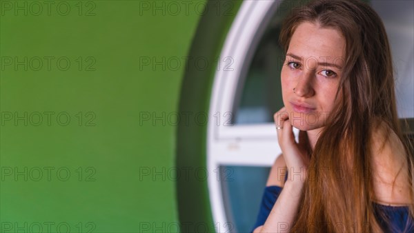 A young pretty red-haired Caucasian woman smiling in a blue dress next to a white sale of a green house