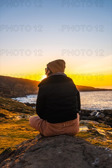 A young woman with a wool cap relaxed in winter watching the sunset on the Jaizkibel mountain in the town of Pasajes