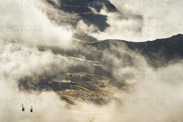 View of the mountain station of the Nebelhorn cable car. Sunshine and low-hanging fog clouds