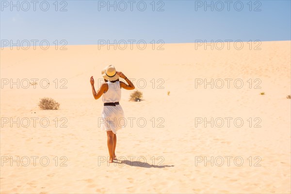 Tourist in white dress and hat walking through the dunes of the Corralejo Natural Park