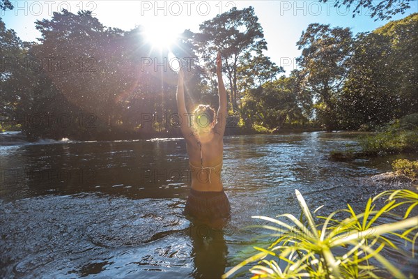 A young woman with her arms up in the Pulhapanzak waterfall on Lake Yojoa. Honduras