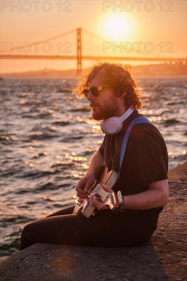 Hipster street musician in black playing electric guitar in the street on sunset