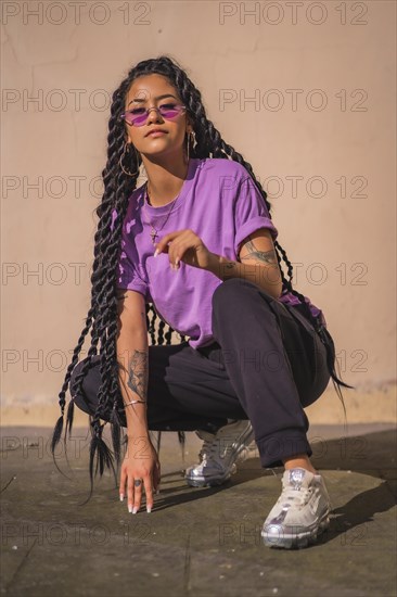 A dark-skinned young woman of Latin ethnicity with purple glasses in an urban session