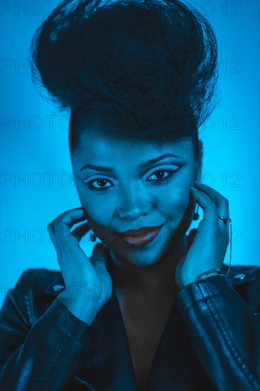 A closeup of a cool fashion hipster girl in a black leather jacket posing at the camera in blue lights