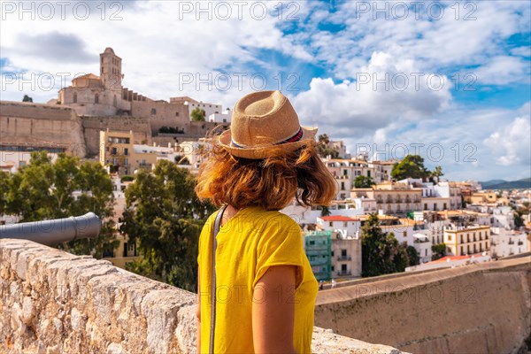 A young woman on vacation looking at the cathedral of Santa Maria de la Neu from the castle wall of Ibiza