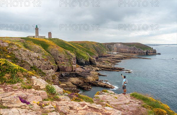 A young tourist taking a photo on the coast next to the Phare Du Cap Frehel