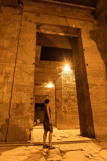 A young girl between the columns at night of the temple of Kom Ombo in traditional dress