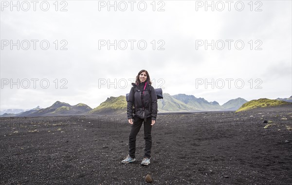 A young woman in volcanic ash and a green mountain in the background on the 54 km trek from Landmannalaugar