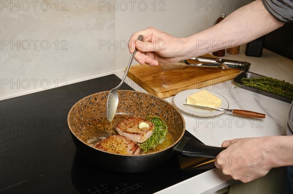 A man pours melted butter over a beefsteak in a frying pan