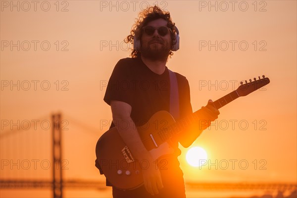 Hipster street musician in black playing electric guitar in street outdoors on sunset