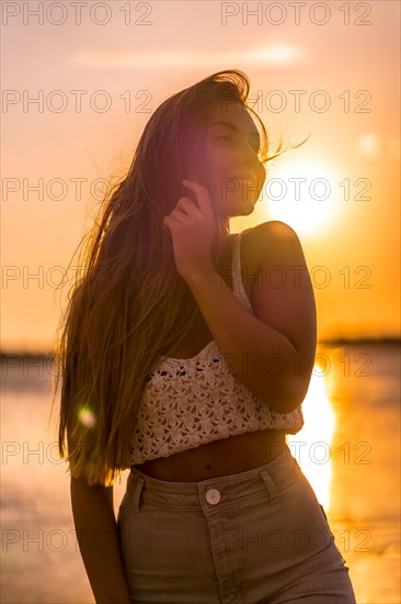 Summer lifestyle. A young blonde Caucasian woman in a white short wool sweater on a beach sunset