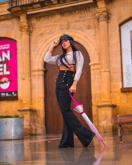 Posing of a young brunette Latina with a leather hat and black pants enjoying an autumn rainy day