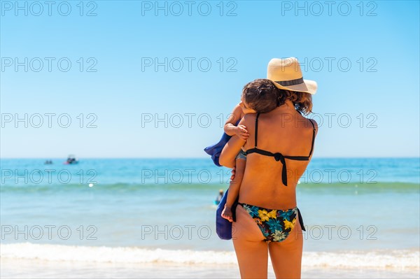 Mother with hat with her son embraced by the sea