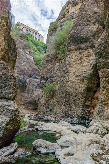 Riverbed under a cliff with a majestic building on top and a blue sky with clouds