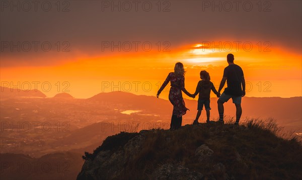 Mother and father next to her son looking at the horizon in a beautiful sunset on the mountain. Adventure lifestyle A summer afternoon in the mountains of the Basque country