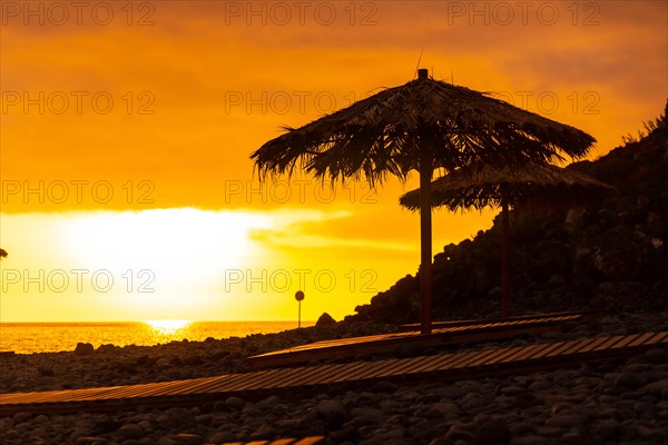 Orange sunset on the umbrellas at Ponta do Sol beach