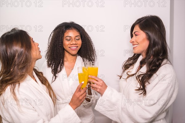 Studio photo with white background of three multi-ethnic friends in bathrobe toasting with healthy juice
