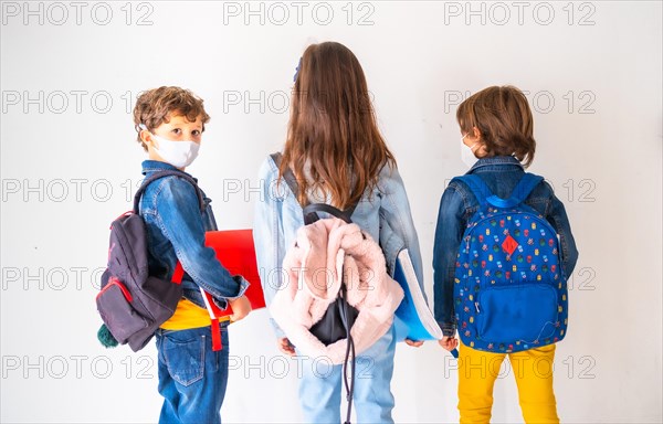 Three children with face masks ready to go back to school. New normality