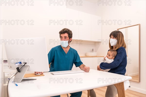 Doctor using a computer to show the medical report to a mother with baby in arms in a hospital