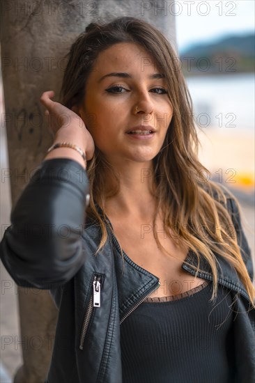 Lifestyle in the city with a blonde girl in white pants and a leather jacket near the beach. Close-up portrait