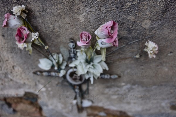 Artificial roses behind a cross on a weathered wall on a grave in a cemetery