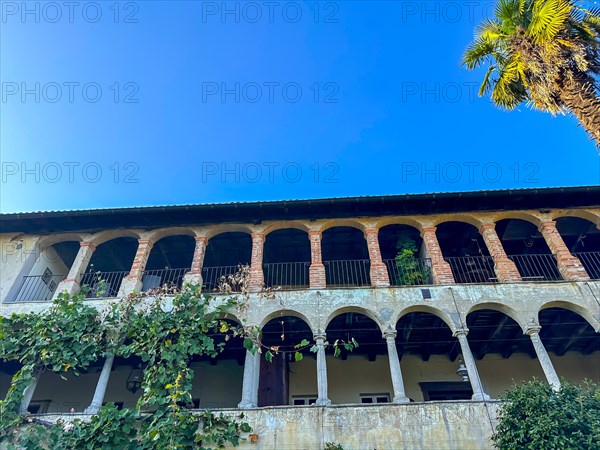 Old Building with Arches and a Palm Tree Against Blue Clear Sky in a Sunny Day in Malcantone