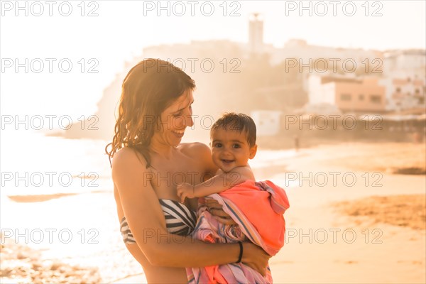A young mother with her six-month-old baby enjoying a sunset on a beach