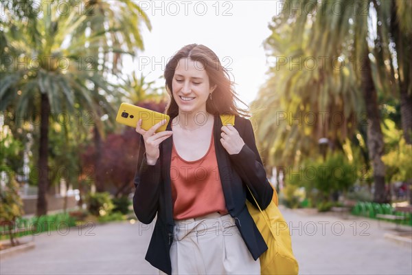 Casual woman sending a voice message walking along an urban park