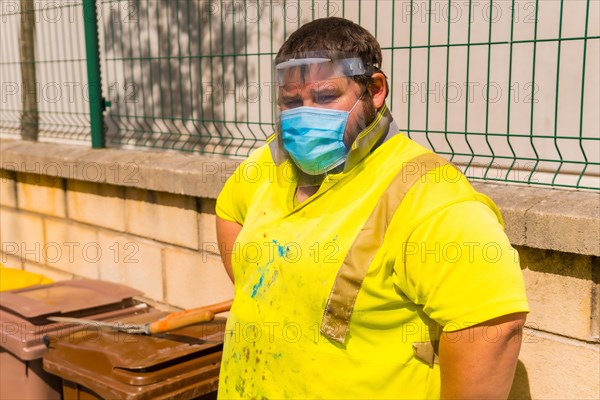 Worker in a recycling factory or clean point and garbage with a face mask and plastic protective screen