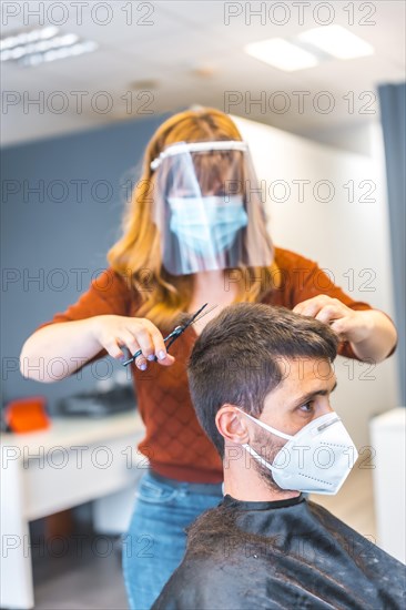 Hairdressers after the Coronavirus pandemic. Caucasian hairdresser with face mask and protective screen