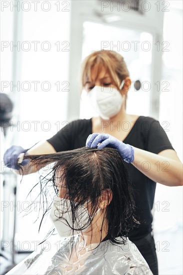 Hairdresser with mask and gloves combing the client. Reopening with security measures of Hairdressers in the Covid-19 pandemic