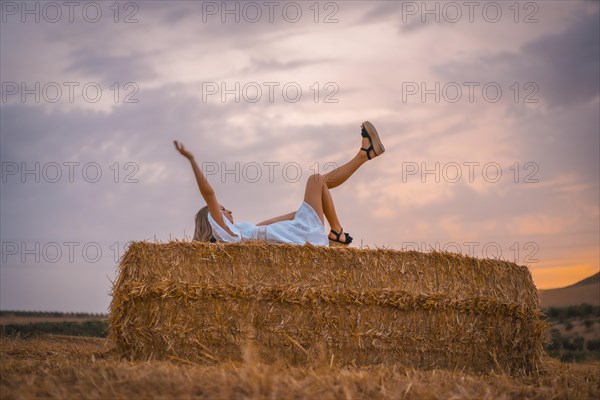 A young blonde Caucasian woman in a white dress in a field of dry straw atop a haystack. In a dry cultivated field in Navarra