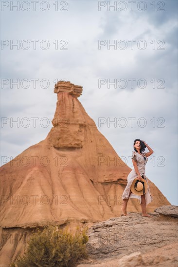 Brunette Caucasian girl in an explorer outfit with a white dress and a straw hat in a beautiful desert on a cloudy afternoon