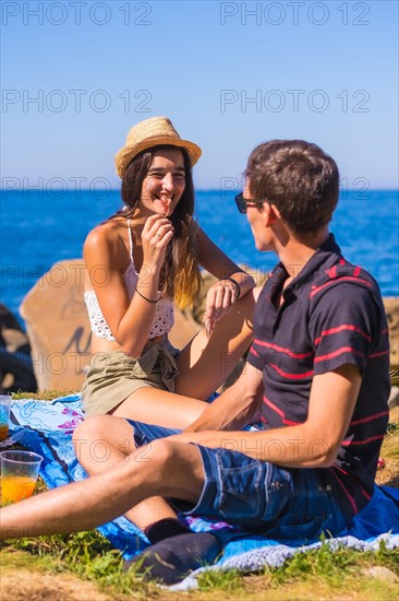 A young Caucasian couple eating some ham at the picnic in the mountains by the sea enjoying the heat