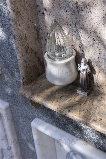 Monk figure next to an electric candle on a grave in a cemetery