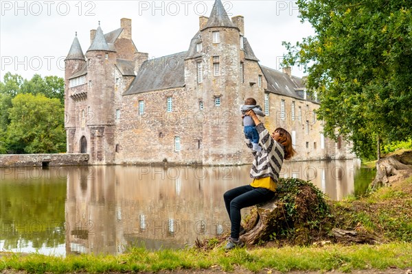 A young mother with her baby visiting the medieval Chateau Trecesson by the lake