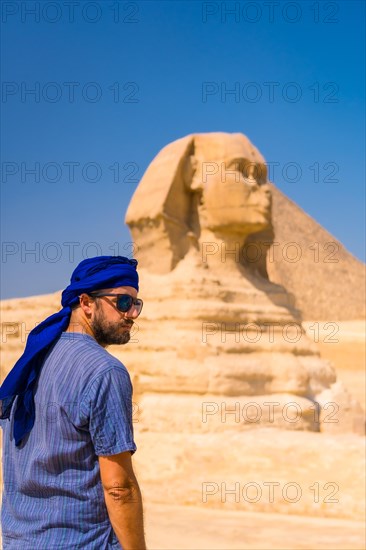 A young tourist enjoying and admiring the Great Sphinx of Giza dressed in blue and a blue turban. Cairo